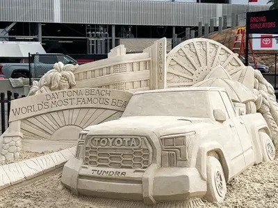 A photo of a marketing sand sculpture for the Toyota Tundra. the sand sculpture includes a beautifully rendered depiction of “Daytona Beach; World's most famous beach” as a sign arching over a sunset points out.